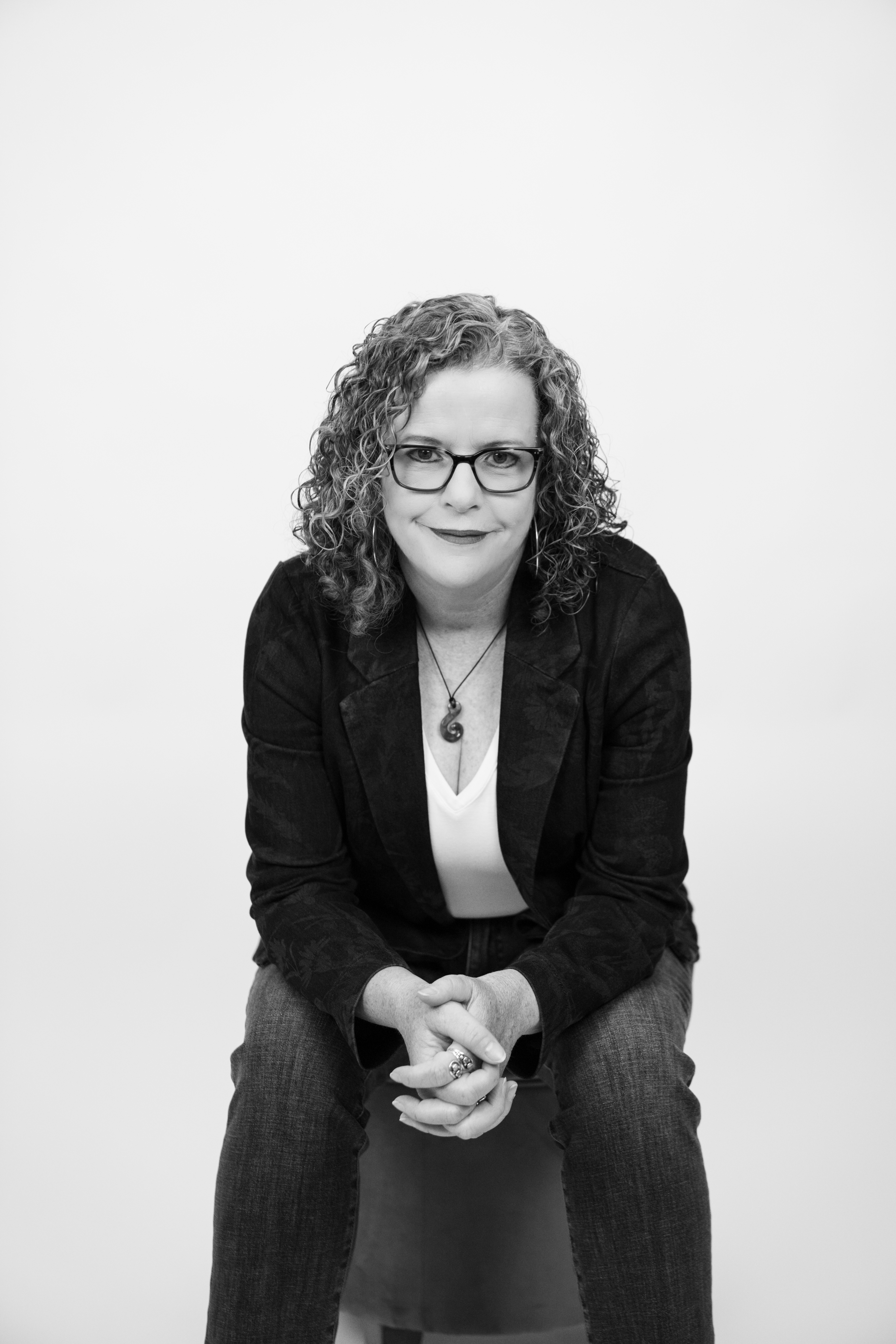 A closeup of Master Maker Podcast host, Leigh O'Donnell wearing a necklace and red glasses, smiling